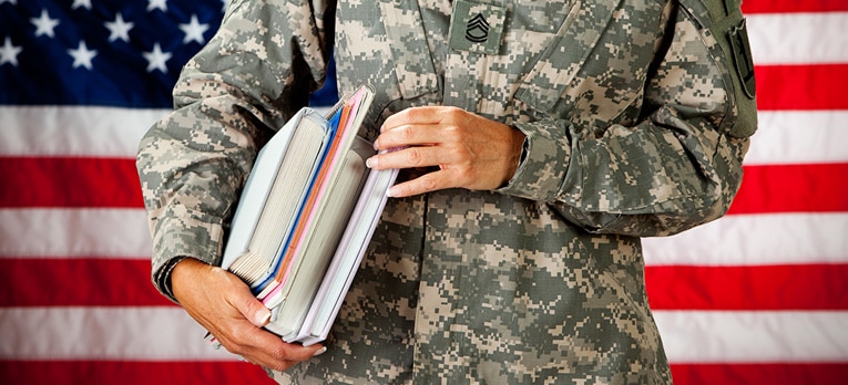 Picture of a person in military fatigues with textbooks in their arms.