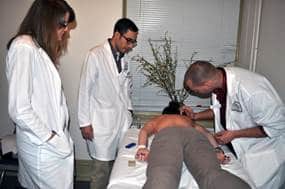 Picture of two student practitioners treating a patient in the student acpuncture clinic with a Clinic Supervisor. 